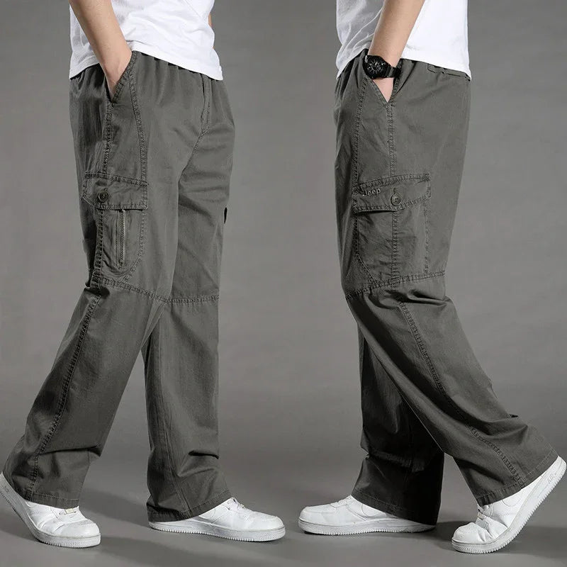 Men wearing loose fit grey cargo pants with multiple pockets and white sneakers on grey background