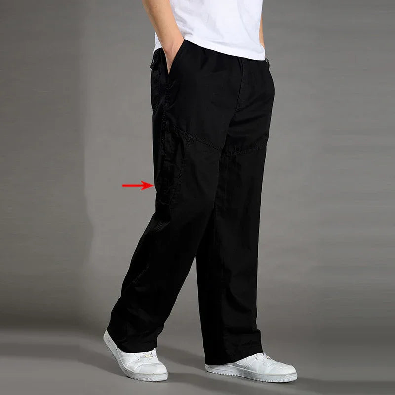 Man wearing black cargo pants with pockets and white sneakers against gray background