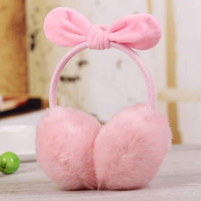 Pink fluffy earmuffs with a soft bow headband on a light wooden surface