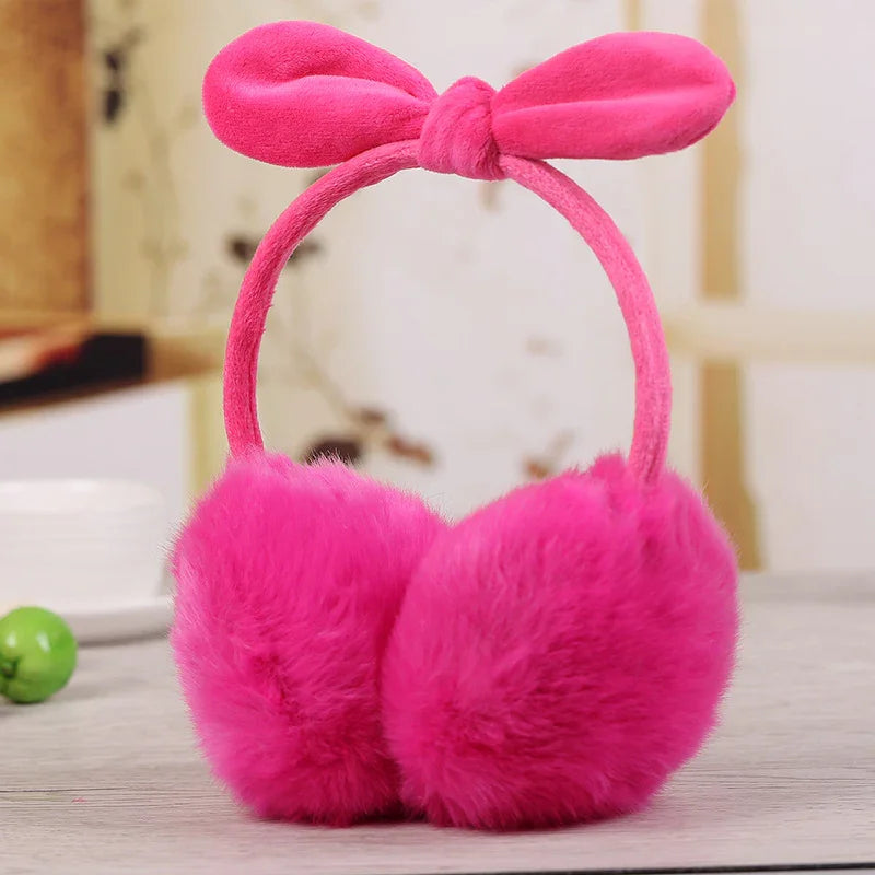 Bright pink fluffy earmuffs with a bow on the headband on a light wooden surface