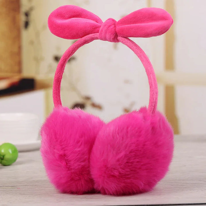 Bright pink fluffy earmuffs with a bow on the headband on a light wooden surface