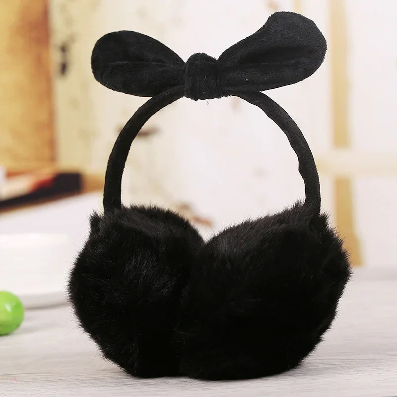 Black fuzzy earmuffs with a bow headband on a light wooden surface