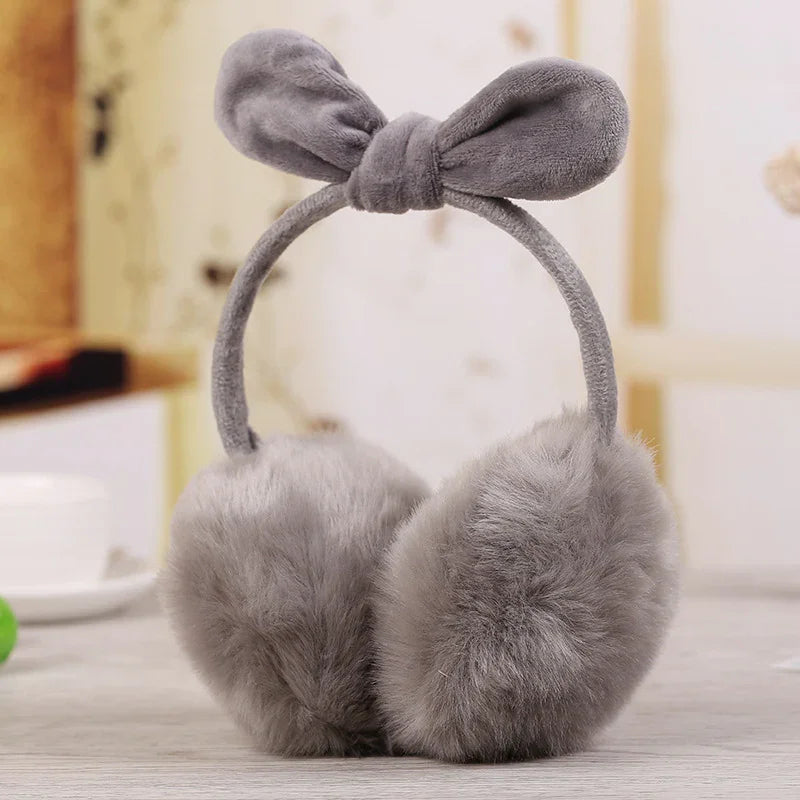 Soft gray fluffy earmuffs with a bow headband on a wooden surface indoors