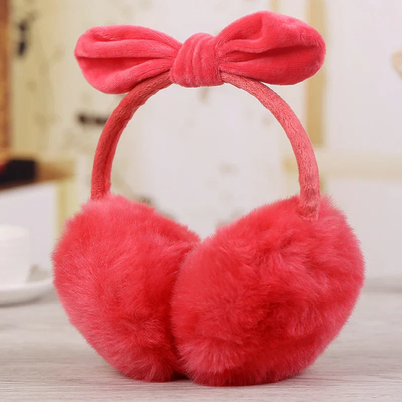 Soft red fluffy earmuffs with a cute bow headband on a light wooden surface