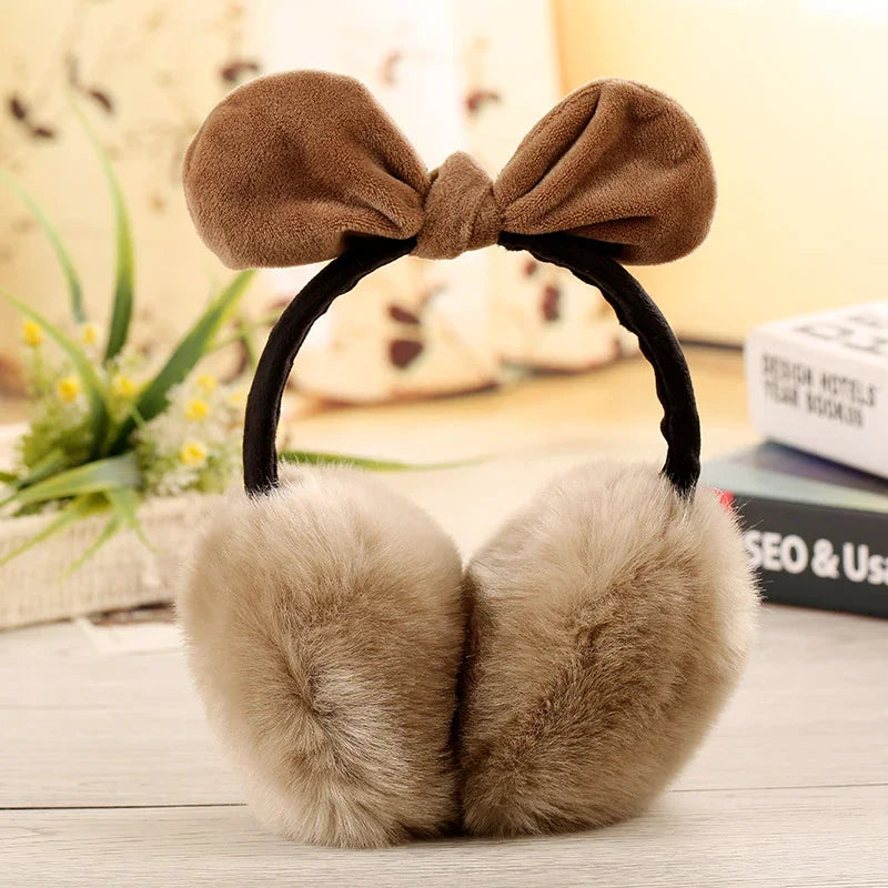 Soft brown faux fur earmuffs with a plush bow headband on a wooden surface
