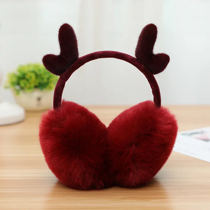 red fluffy earmuffs with reindeer antler design on wooden surface