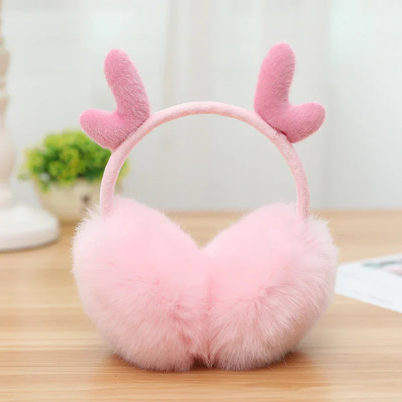 Soft pink fluffy earmuffs with heart-shaped plush decorations on a wooden surface