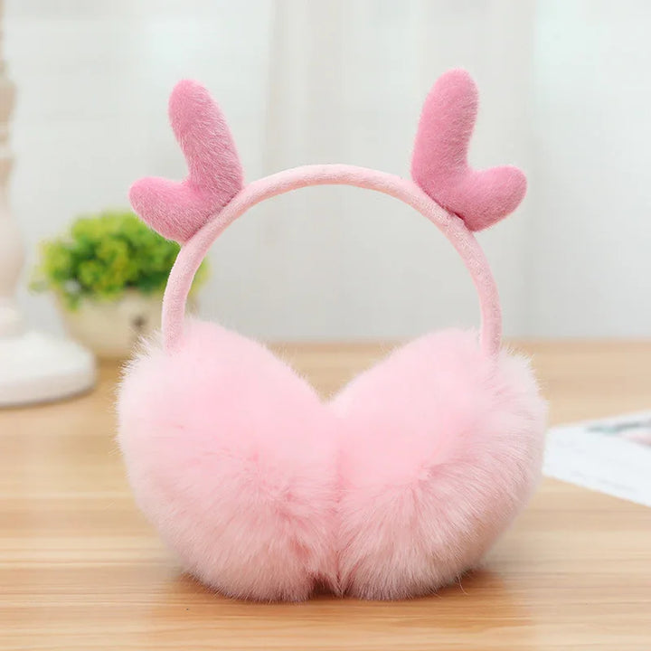 Soft pink fluffy earmuffs with heart-shaped plush decorations on a wooden surface