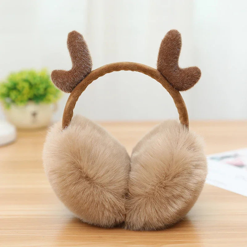 Beige fluffy earmuffs with brown reindeer antlers on wooden table, cozy winter accessory