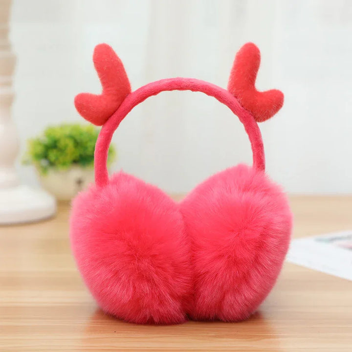 Red fluffy winter earmuffs with heart-shaped antlers on wooden table
