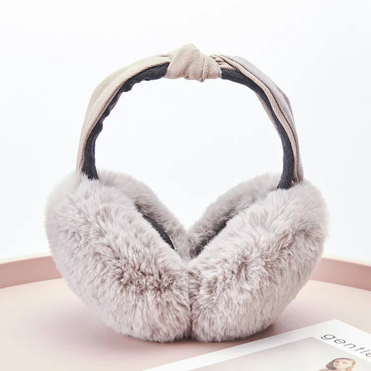 Soft grey faux fur winter earmuffs with twisted beige fabric headband on a round surface