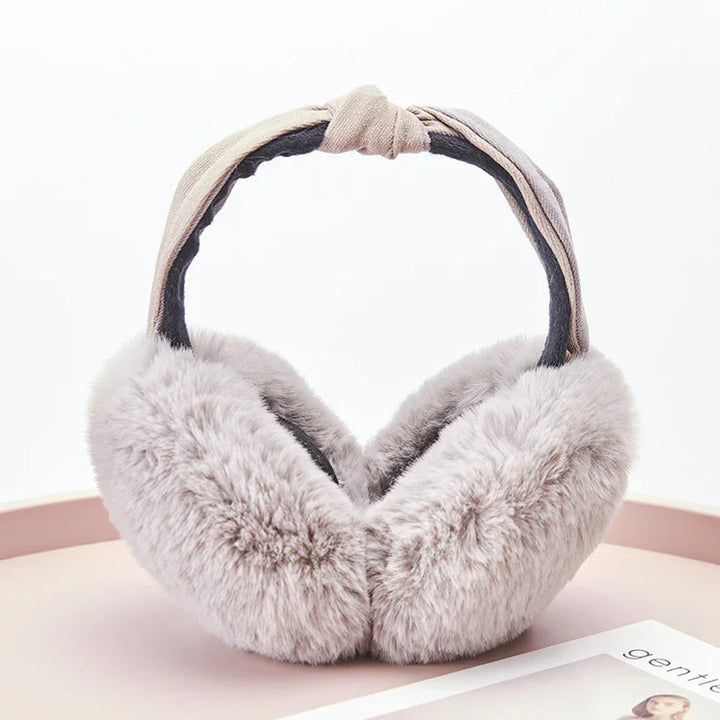 Soft grey faux fur winter earmuffs with twisted beige fabric headband on a round surface