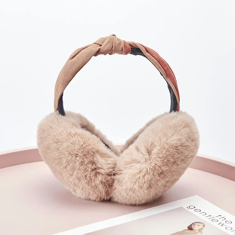 Soft beige faux fur earmuffs with a knotted fabric headband on a pink surface