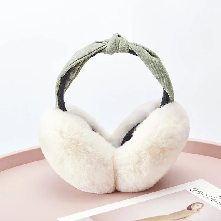 Soft white fluffy earmuffs with a knotted green fabric headband on a pink surface