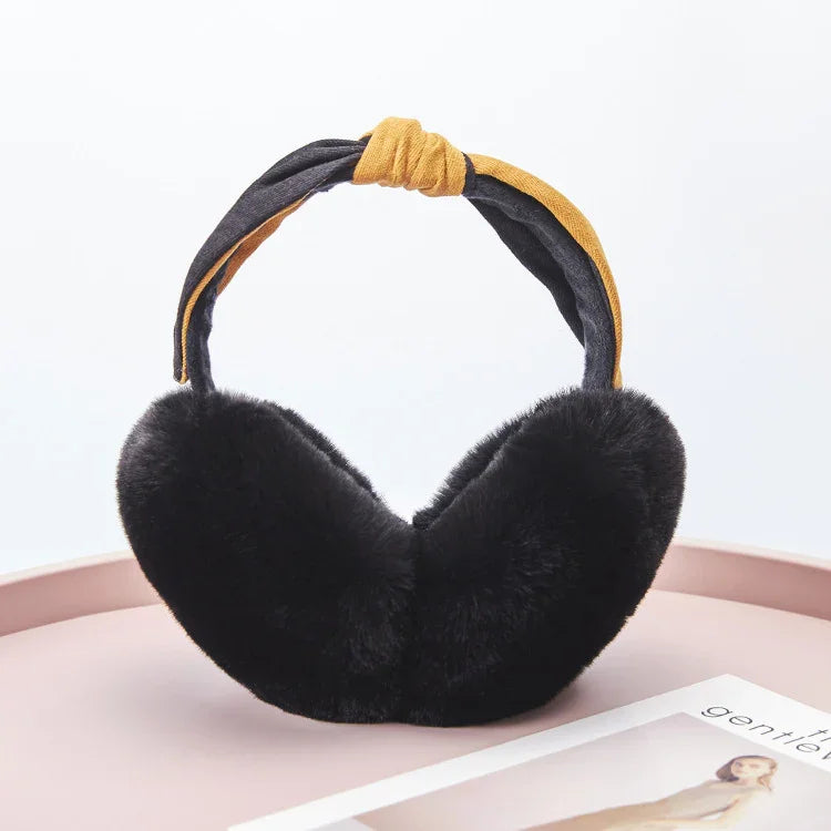 Black faux fur earmuffs with mustard and black fabric headband on pink surface near magazine