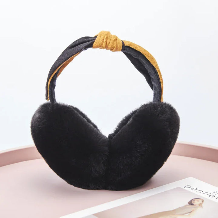 Black faux fur earmuffs with mustard and black fabric headband on pink surface near magazine