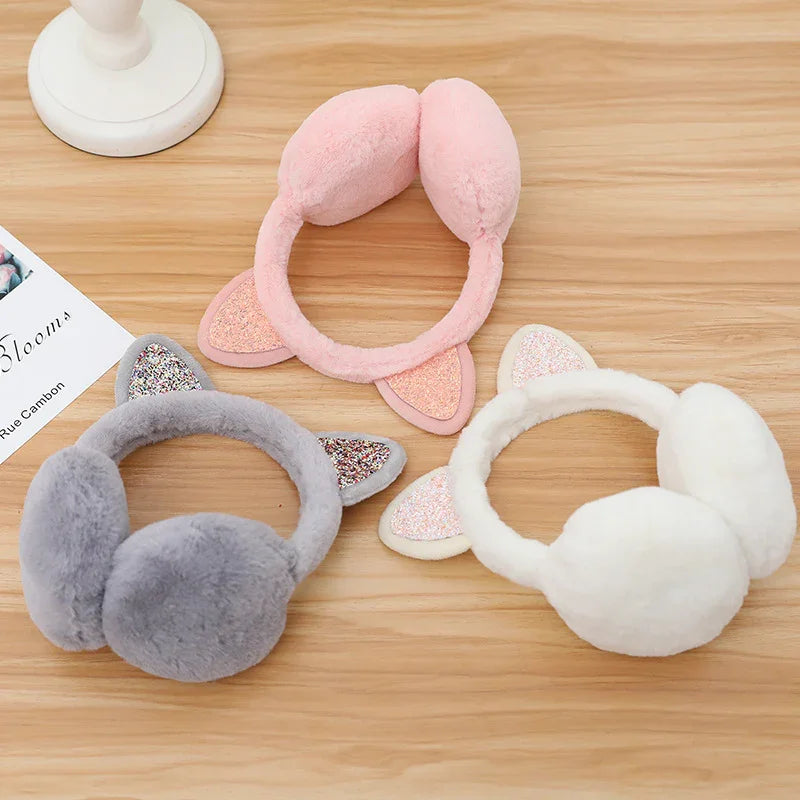 Plush earmuffs in pink, gray, and white with glittery cat ears on wooden table