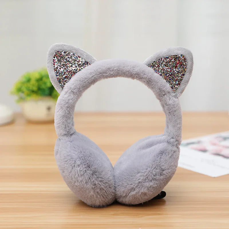 Gray plush earmuffs with glittery cat ears on wooden table with blurred background