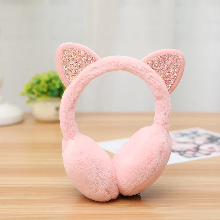 Pink fluffy earmuffs with glittery cat ears on wooden surface and blurred background
