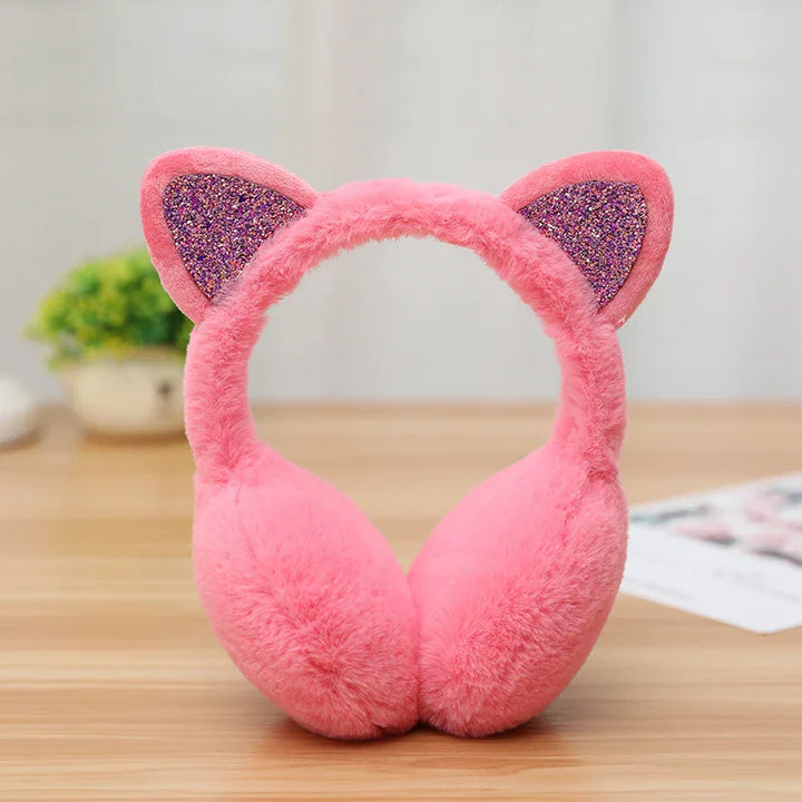 Pink fluffy earmuffs with glittery cat ears on wooden table