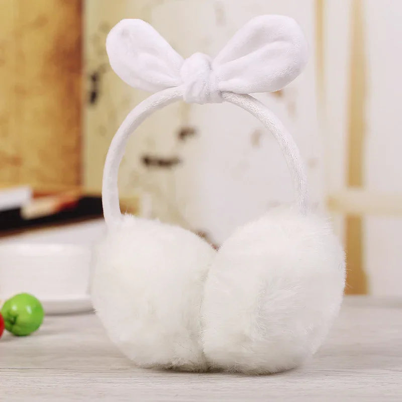 White fluffy earmuffs with a bow headband on a wooden table in a cozy indoor setting