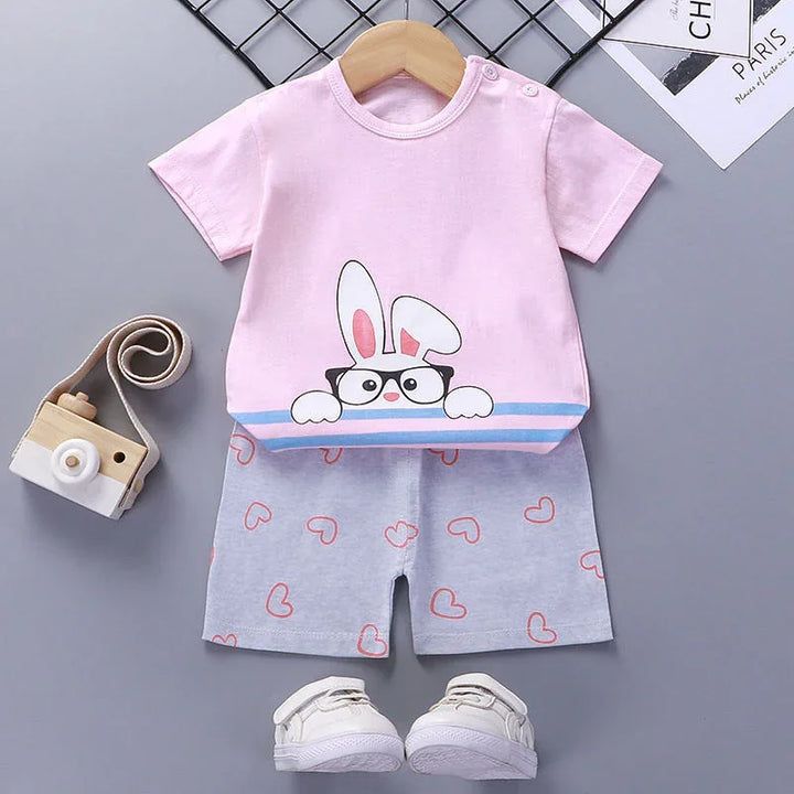 Toddler outfit with pink bunny print t-shirt, gray shorts with heart patterns, and white shoes