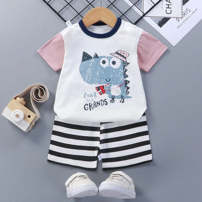 Toddler outfit with dinosaur graphic tee, pink sleeves, striped shorts, white shoes, and wooden toy camera