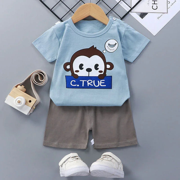 Toddler outfit with blue monkey print t-shirt, gray shorts, white shoes, and wooden toy camera