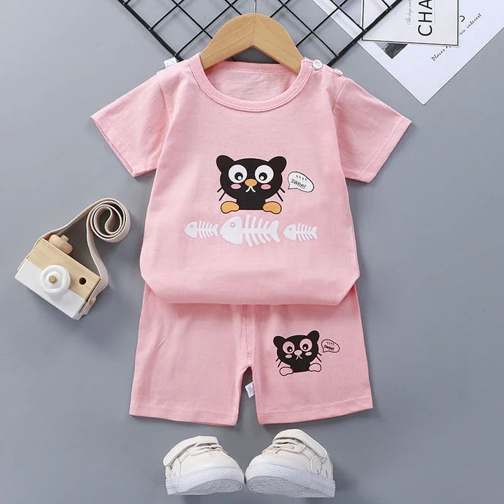 Pink toddler outfit with black cat and fishbone print, matching shorts, and white baby shoes