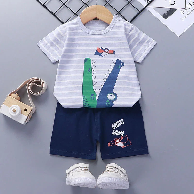 Baby boy outfit with striped crocodile print T-shirt, navy shorts with bird design, white shoes, and wooden toy camera