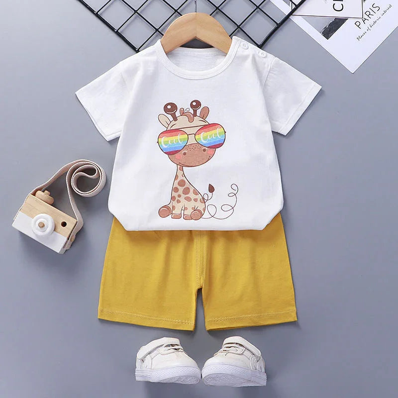 Cute toddler outfit with white giraffe print T-shirt, yellow shorts, white shoes, and a wooden toy camera