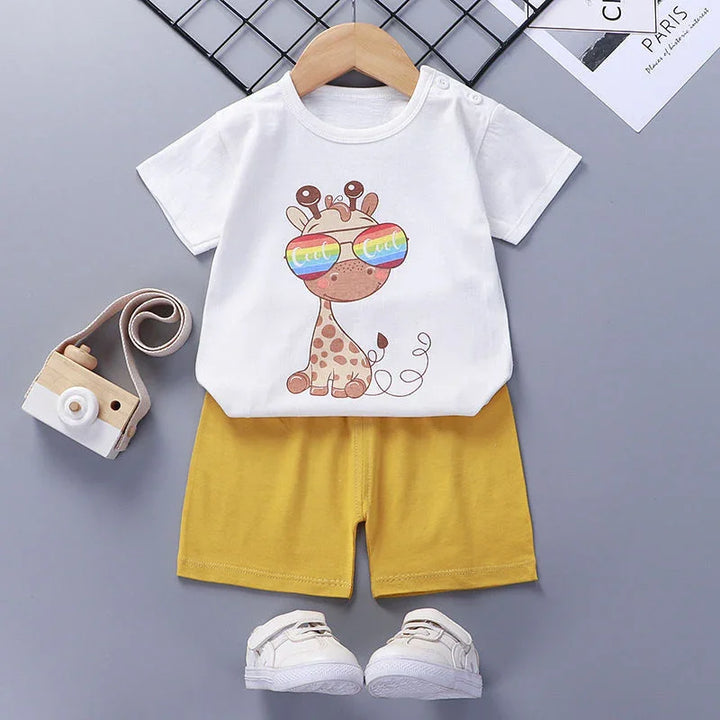Cute toddler outfit with white giraffe print T-shirt, yellow shorts, white shoes, and a wooden toy camera