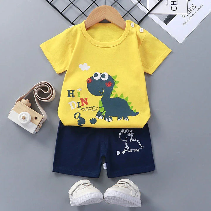Yellow toddler T-shirt with cartoon dinosaur print, navy shorts, white shoes, and wooden toy camera