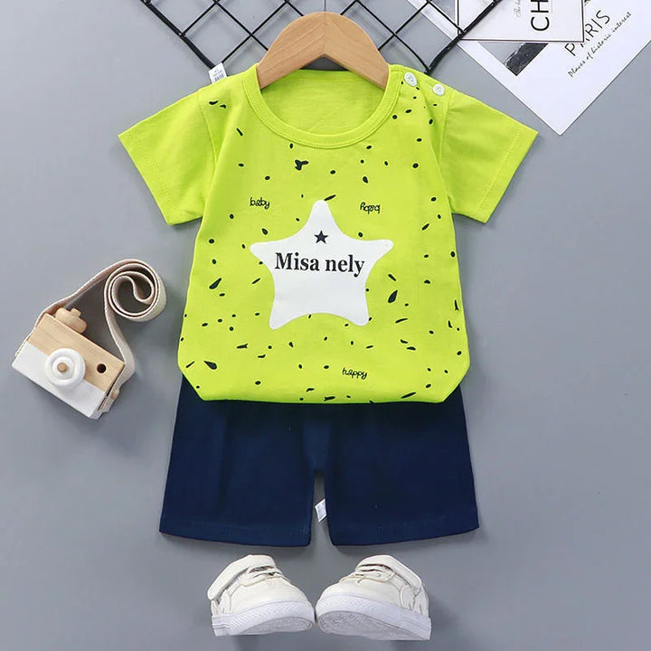 Bright green baby shirt with star print and navy shorts, paired with white baby shoes and wooden toy camera