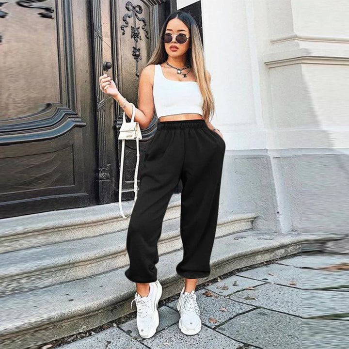 Woman wearing black jogger pants, white crop top, white sneakers, and sunglasses standing on outdoor steps