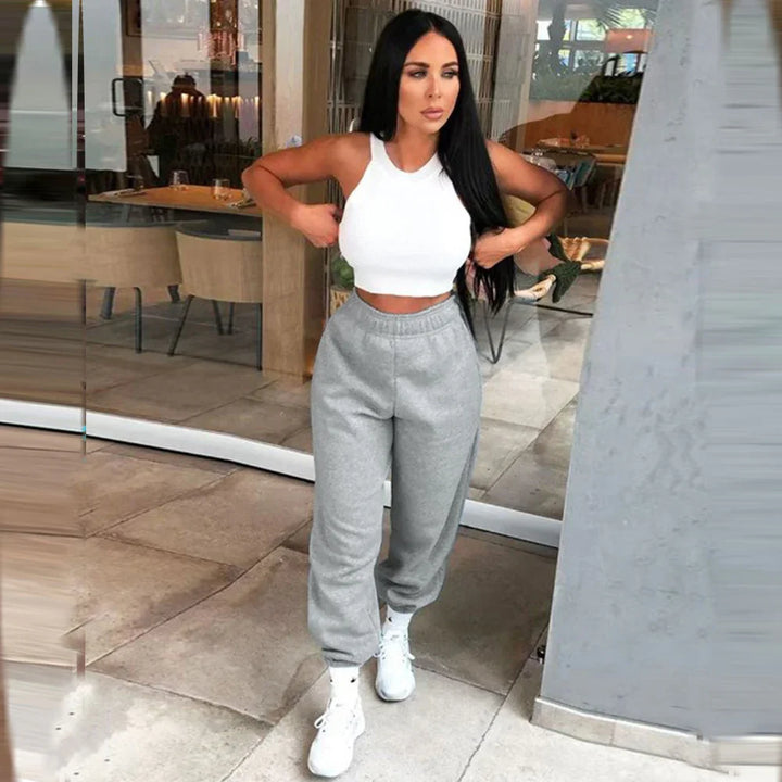 Woman in white crop top and gray sweatpants posing indoors with long black hair and white sneakers