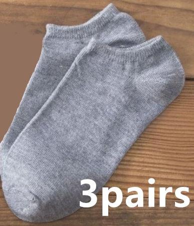 Three pairs of plain grey ankle socks on wooden surface