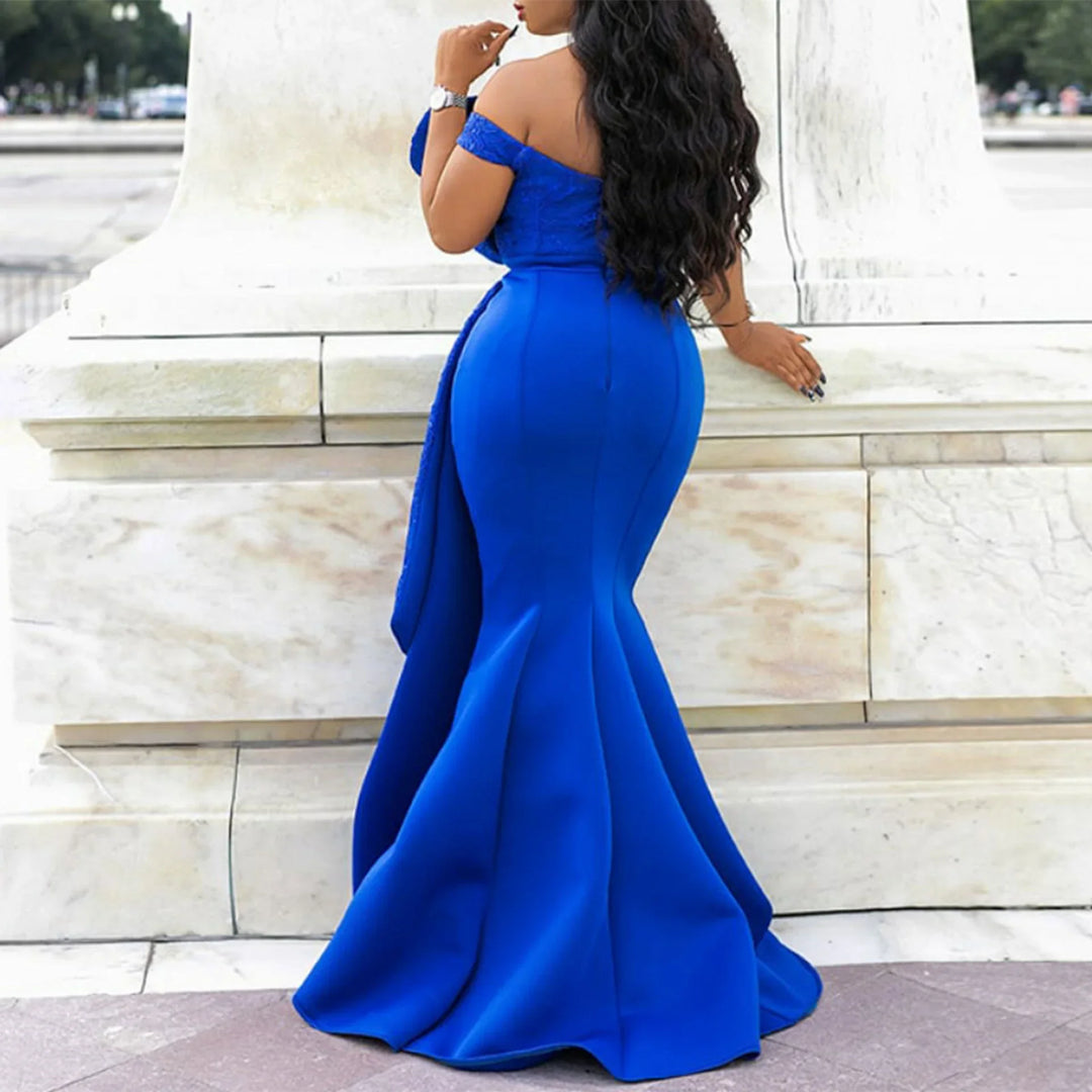 Woman posing in a royal blue off-shoulder mermaid gown with long wavy hair by white stone structure