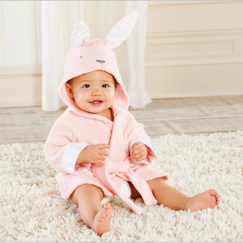 Smiling baby sitting on a fluffy cream rug wearing a soft pink bunny hooded bathrobe