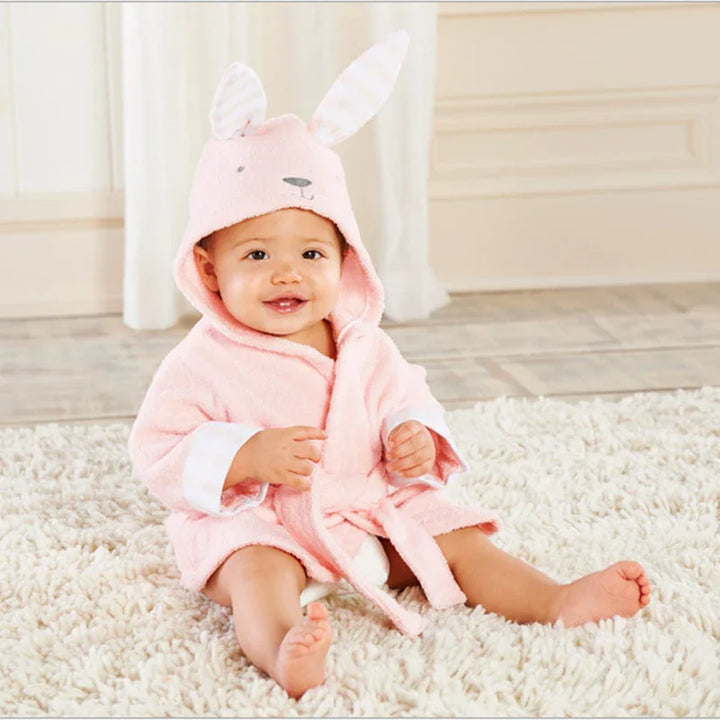 Smiling baby sitting on a fluffy cream rug wearing a soft pink bunny hooded bathrobe
