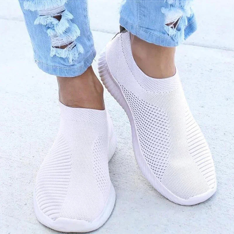 Close-up of white slip-on knitted sneakers worn with light blue ripped jeans on concrete floor
