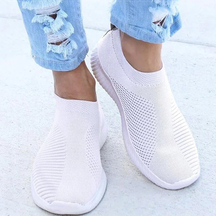 Close-up of white slip-on knitted sneakers worn with light blue ripped jeans on concrete floor