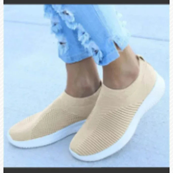 Pair of beige slip-on knit sneakers with white soles worn with distressed light blue jeans