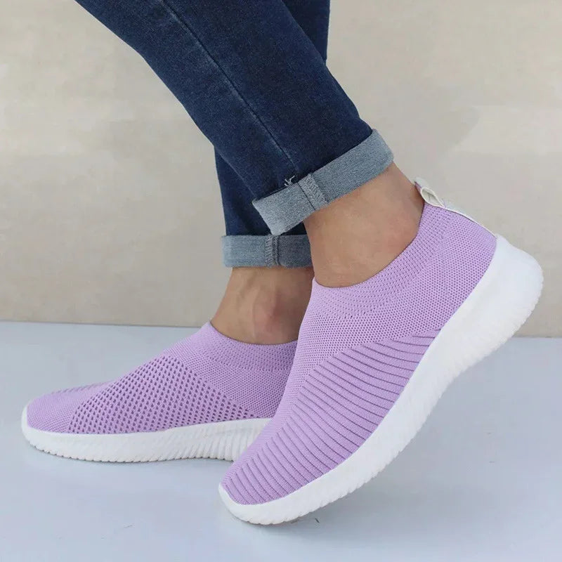 Person wearing lilac slip-on knitted sneakers with white soles and rolled-up dark blue jeans