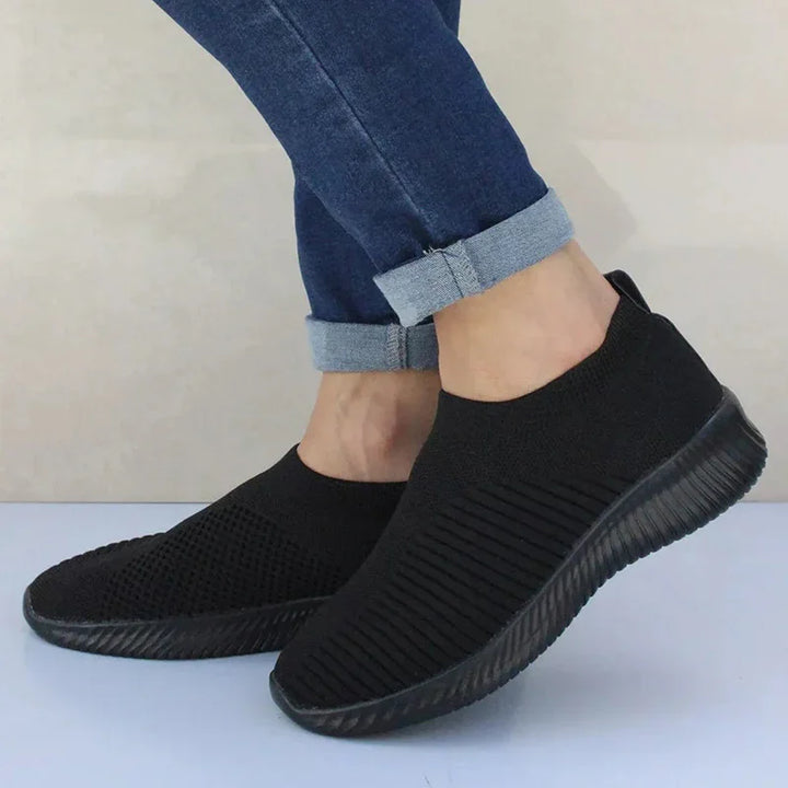 Casual black slip-on sneakers with textured knit fabric worn with rolled-up blue jeans