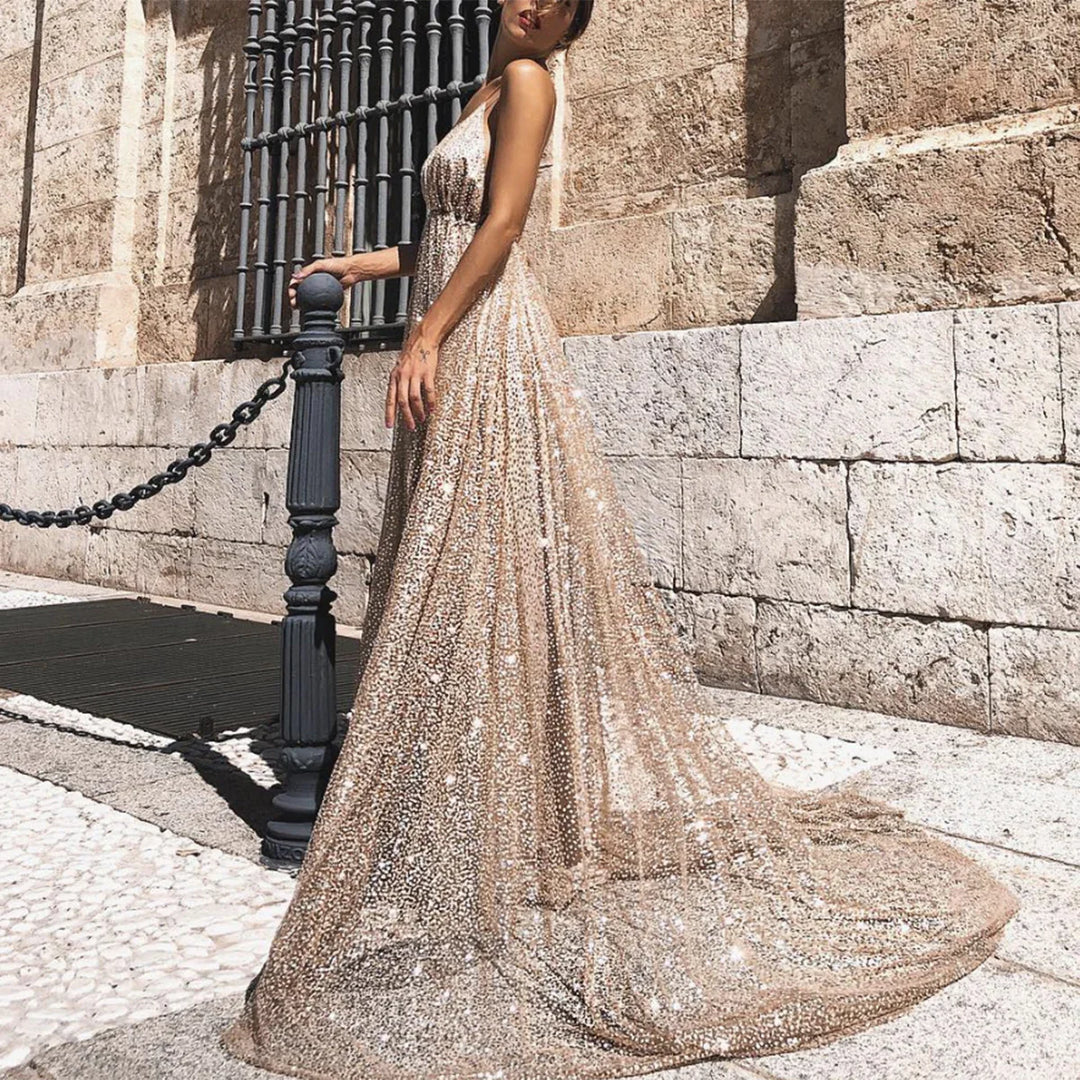 Woman wearing sparkling gold sequin gown standing by black chain post against stone wall