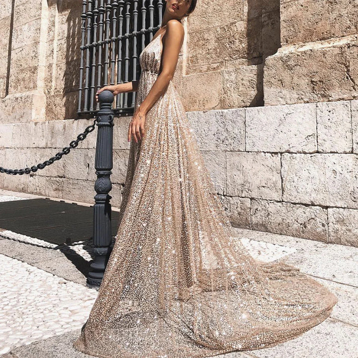 Woman wearing sparkling gold sequin gown standing by black chain post against stone wall