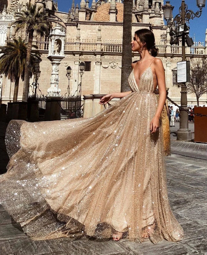 Woman in sparkling beige sequin gown posing outdoors near historic stone building and palm trees