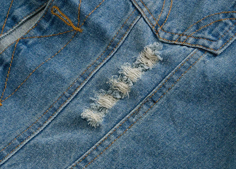 Close-up of blue denim fabric with orange stitching and a vertical distressed rip detail