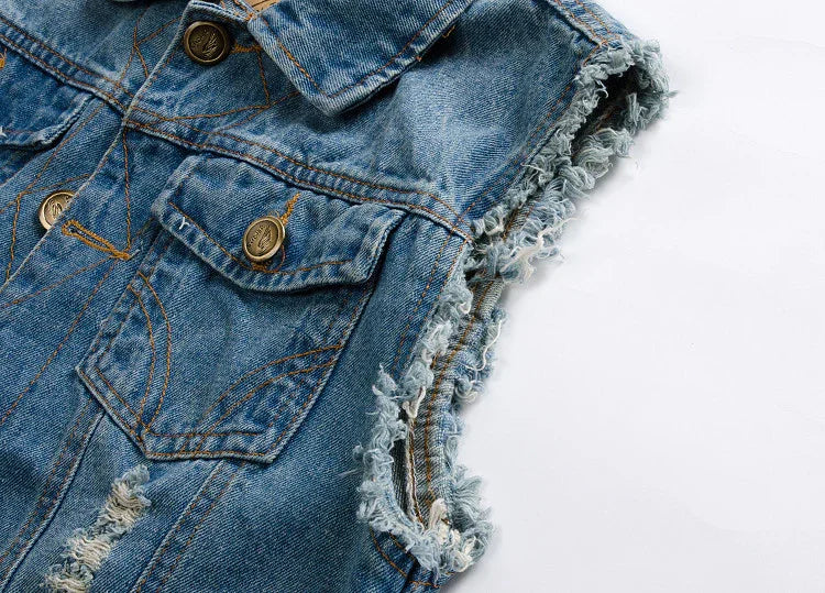 Close-up of a blue distressed denim vest with frayed armholes and brass buttons on white background